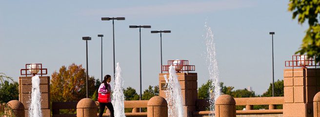 A person walking past the Queens College Fountain (Cooperman Plaza).