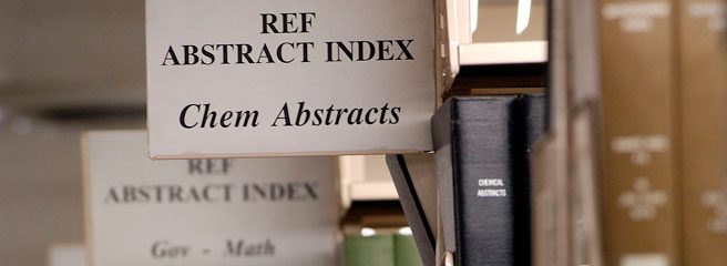 A close-up of the bookshelf aisle contents sign. The sign in the foreground reads: Ref Abstract Index Chem Abstracts. The sign in the background reads: Ref Abstract Index Gov-Math.