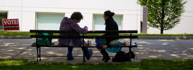 Two people sitting on a bench outside.