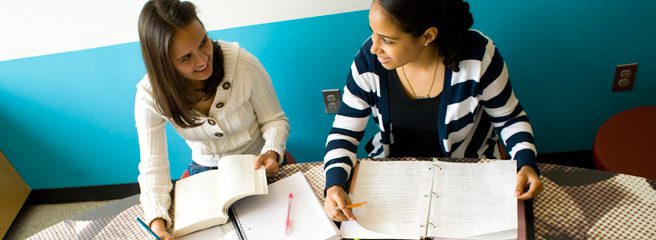 Two people sitting at a table with their notebooks open and studying.