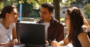 Three people having a conversation while sitting in front of a laptop.