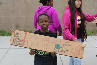 A child holding up a sign that reads: Earth hates plastic trash