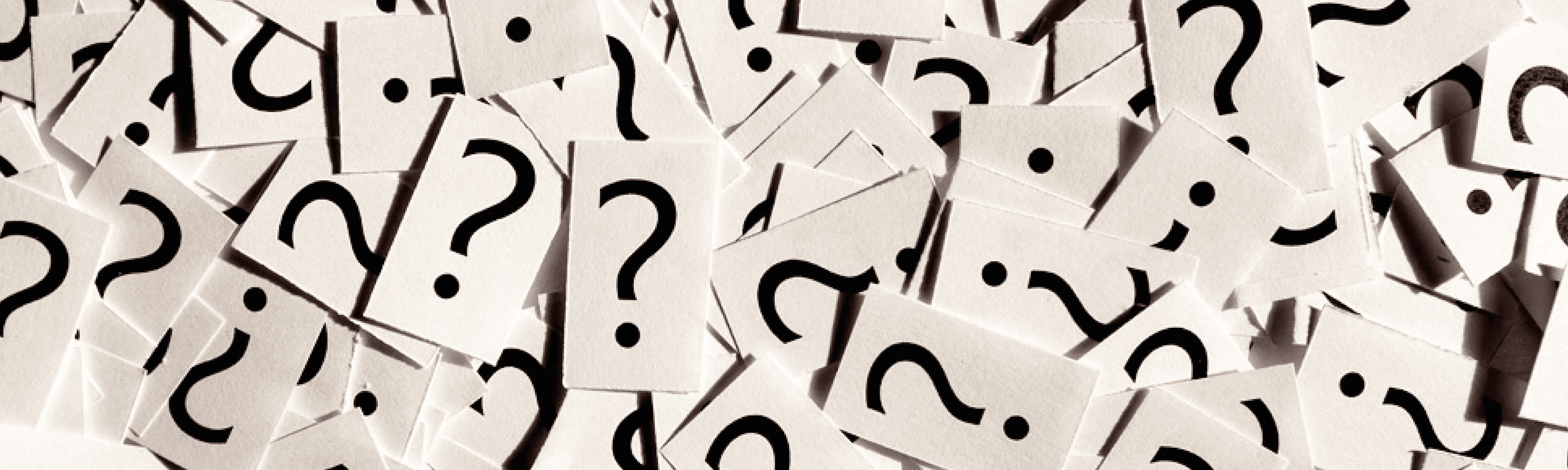Scattered overlapping papers with questions marks. Scattered overlapping papers with questions marks.