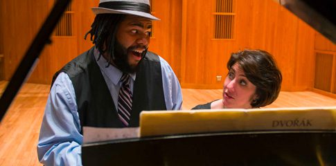 Joseph Hill sings while sitting next to a person who is playing the piano.