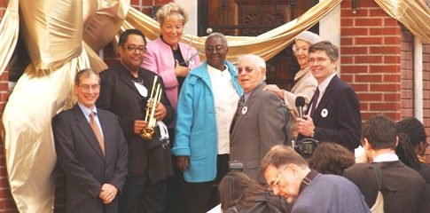 The Gift of Armstrong's Legacy: Michael Cogswell (far left) gathers with jazz great Jon Faddis (second from left), and college and community officials on the steps of Louis Armstrong’s Corona residence at the October 15, 2003 ribbon-cutting ceremony to open the house as a museum. Queensborough President Helen Marshall (in pink jacket) helped cut the ribbon. At far right is Queens College President James L. Muyskens.