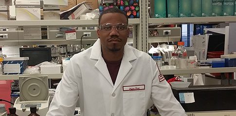 Olivier Noel standing in a lab while wearing a lab coat and protective glasses.