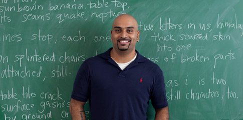 Rajiv Mohabir stands in front of a blackboard.