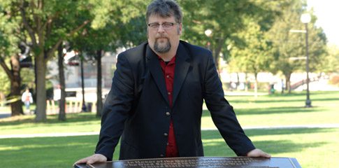 Professor Bobby A. Wintermute stands at the Queens College World War II Veterans Memorial Plaza. 