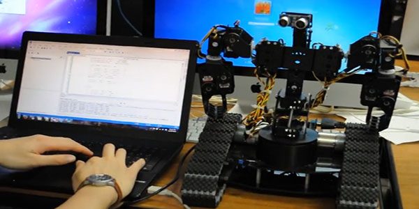 A close-up of a laptop on the left-hand side and a robot on the right-hand side of a table.