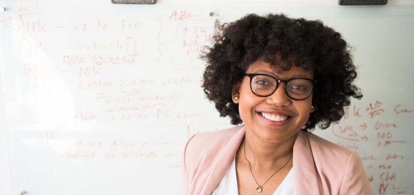 A person smiling at the camera in front of a whiteboard.