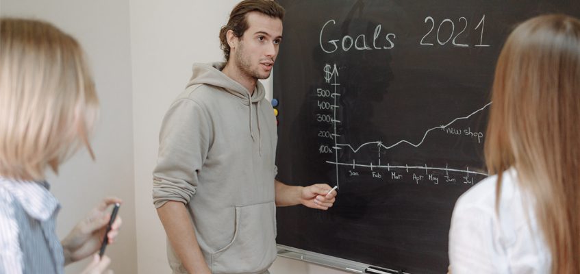 A person presents their graph which is drawn on a chalkboard to two people observing.