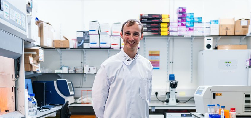 A person in a lab coat standing inside a lab.