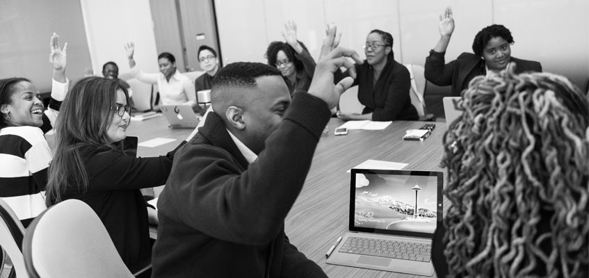 A group of people sitting at a table with their hands raised.