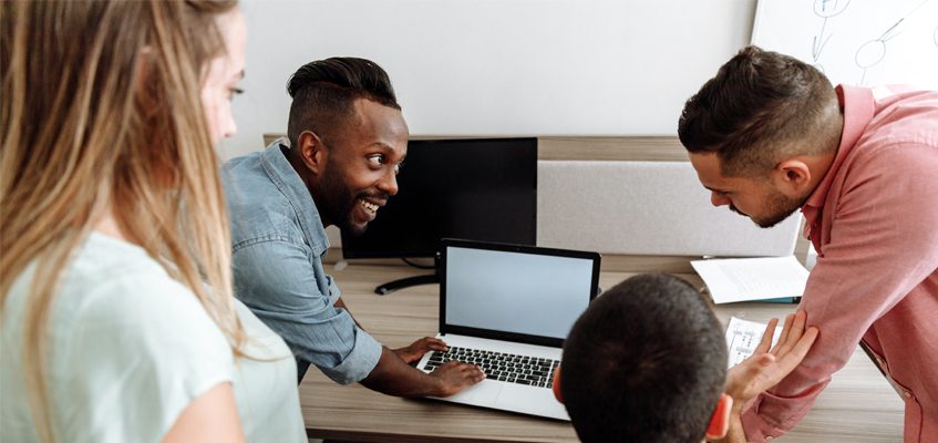 Four people gathered around a laptop on a table.