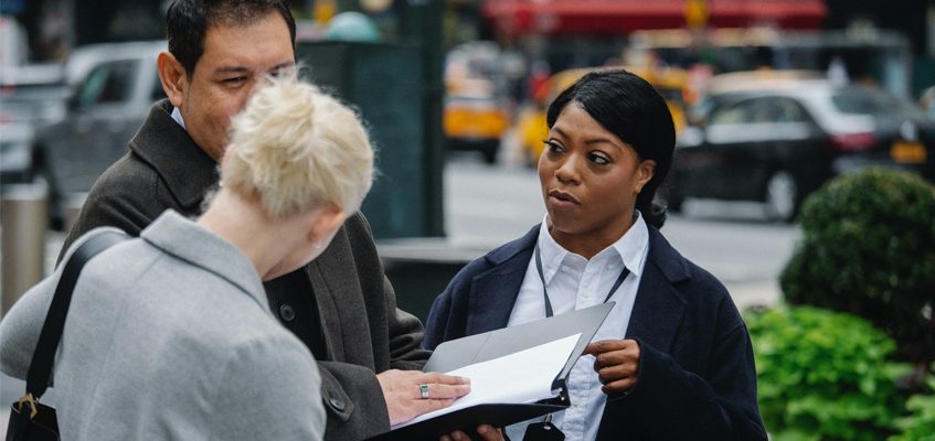 A person with an open binder standing and talking to two other people.