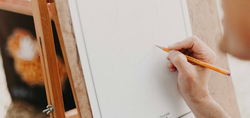 A close-up of a person’s hand drawing with a pencil on a piece of paper.