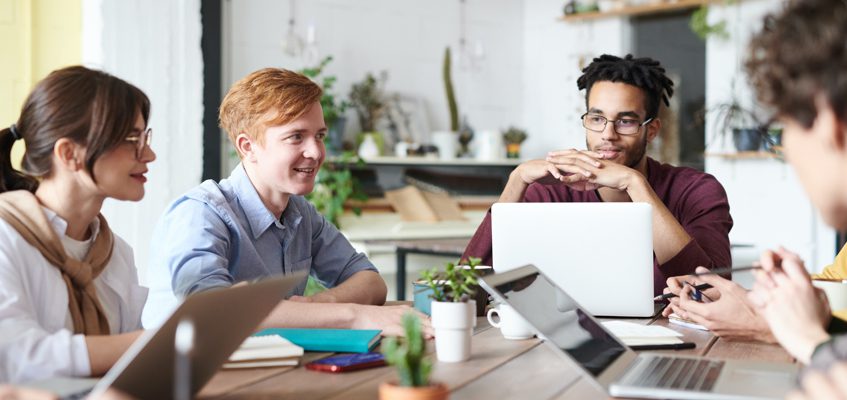 A group of people sitting at a table with laptops and notebooks.