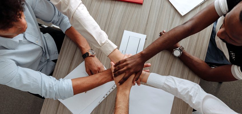 Five students huddled around a table with stacked hands.