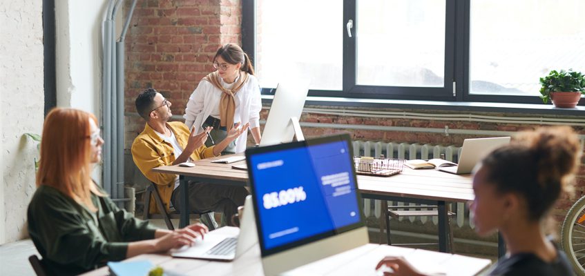 Four people sitting on laptops/computers in an office setting.