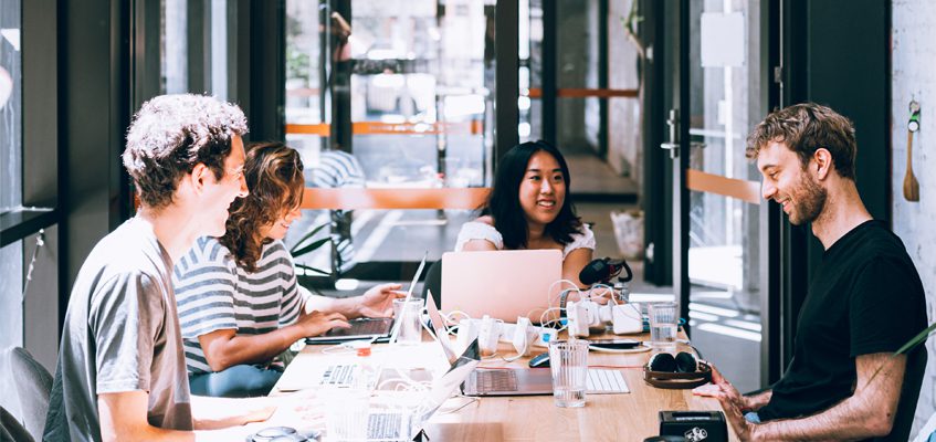 Four people sit at a table working on their laptops.