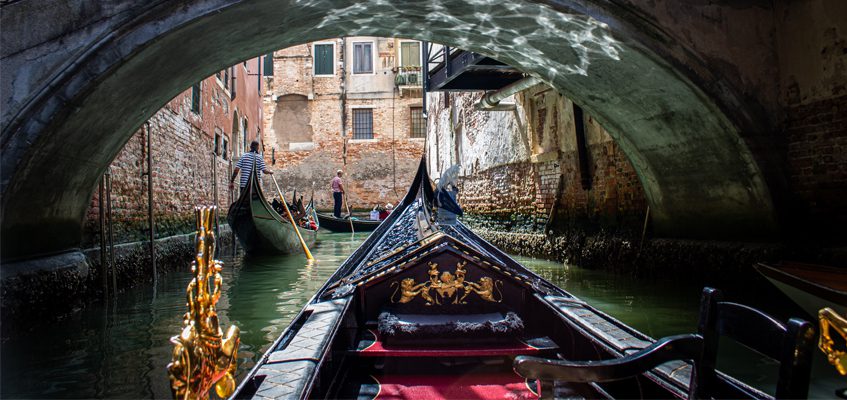 The view from a gondola on the water passing under a small bridge.