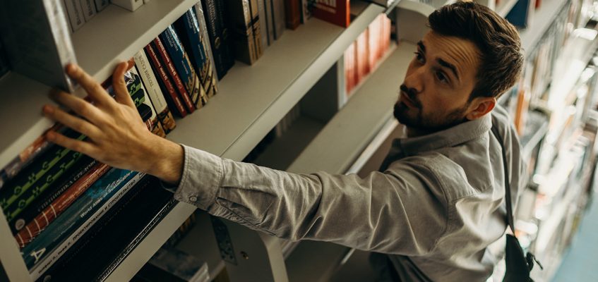 A person reaching out to grab a book from a shelf.