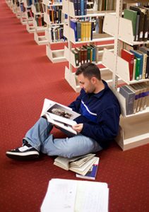 A person sitting on the floor of the library reading books.