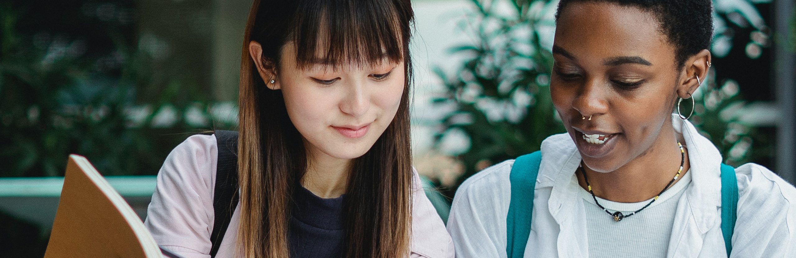 Two female students sitting next to each other looking at a notebook.