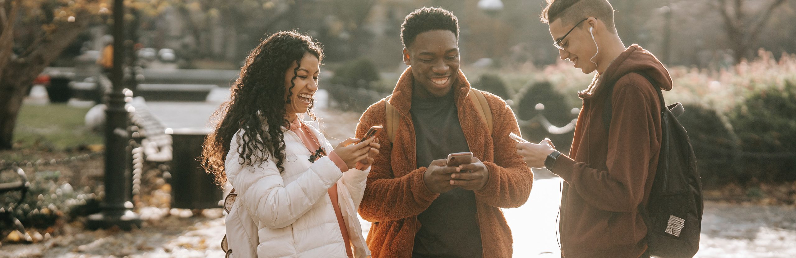 Three students in a park laughing and looking at their phones.