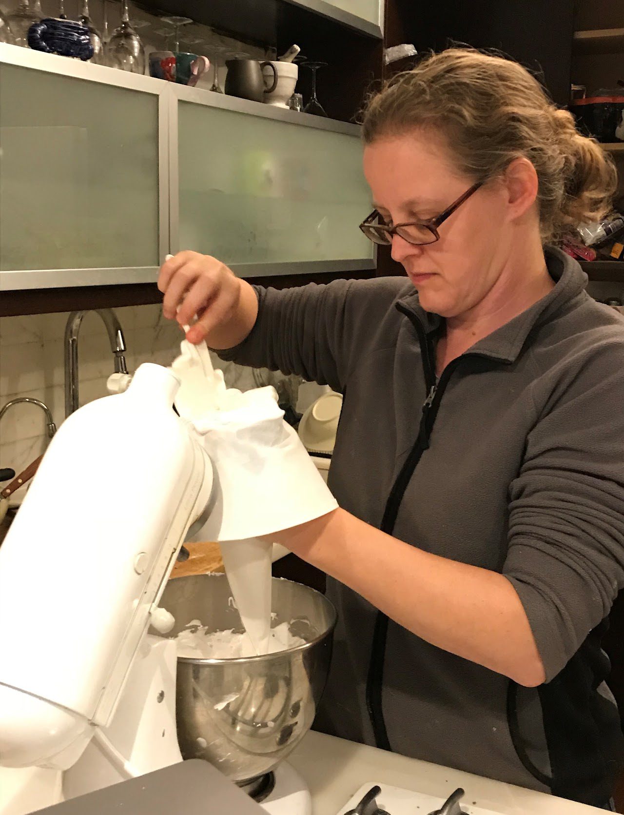 Nathalia Holtzman scooping frosting from a mixer to a pastry piping bag.