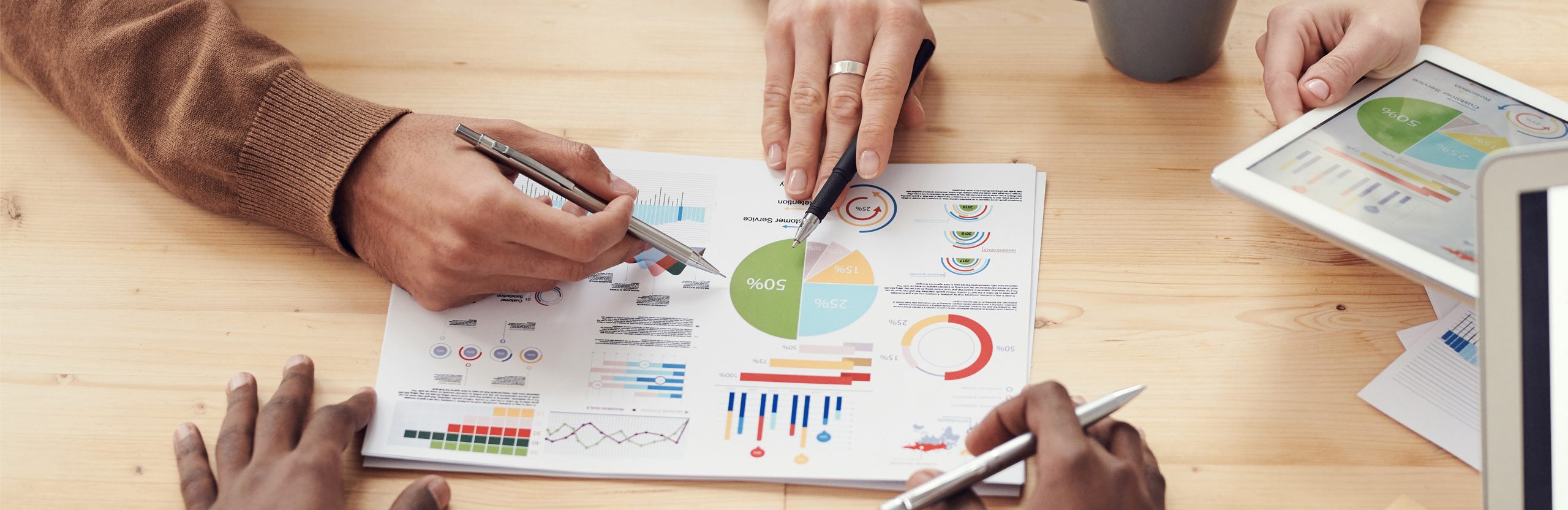 People’s hands holding pens pointing to a paper with graphs.