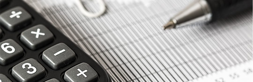 A close-up of a calculator, a pen, and a paperclip on thinly lined paper.