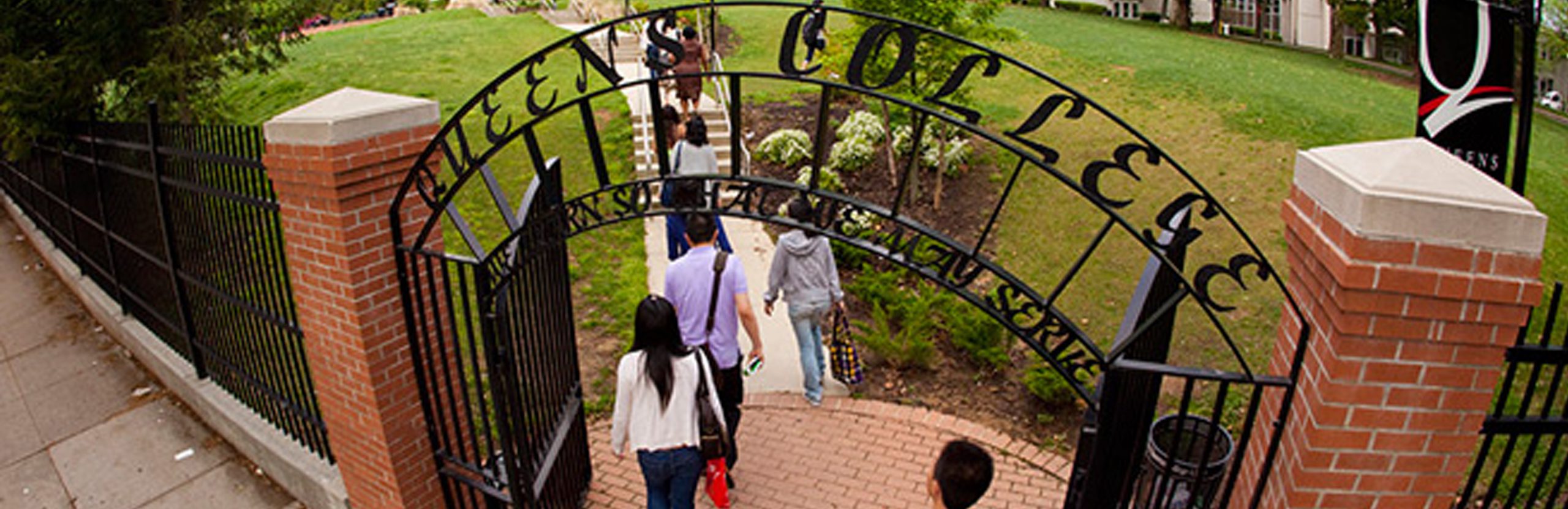 People walking into Queens College through the main gate.