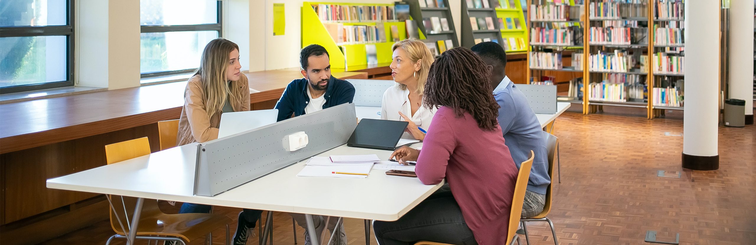 Five students sitting at a table in a library. 