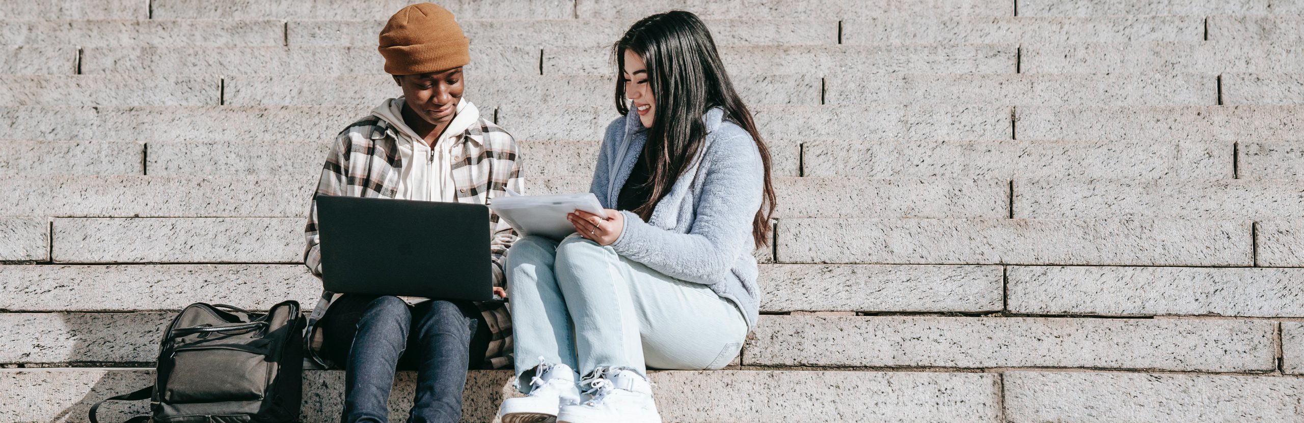 Two students sitting on steps working together with a laptop.