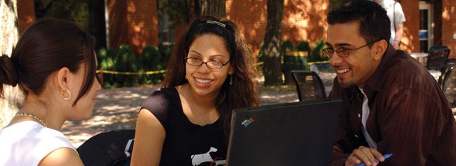Two students looking at a laptop while sitting on the grass. 
