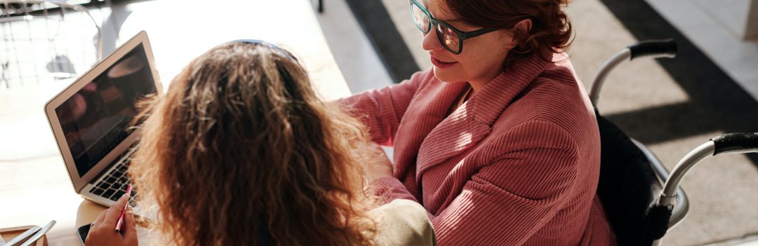 Two women sitting at a table with a laptop.