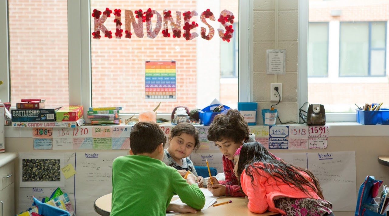 Four elementary students writing notes in their classroom.