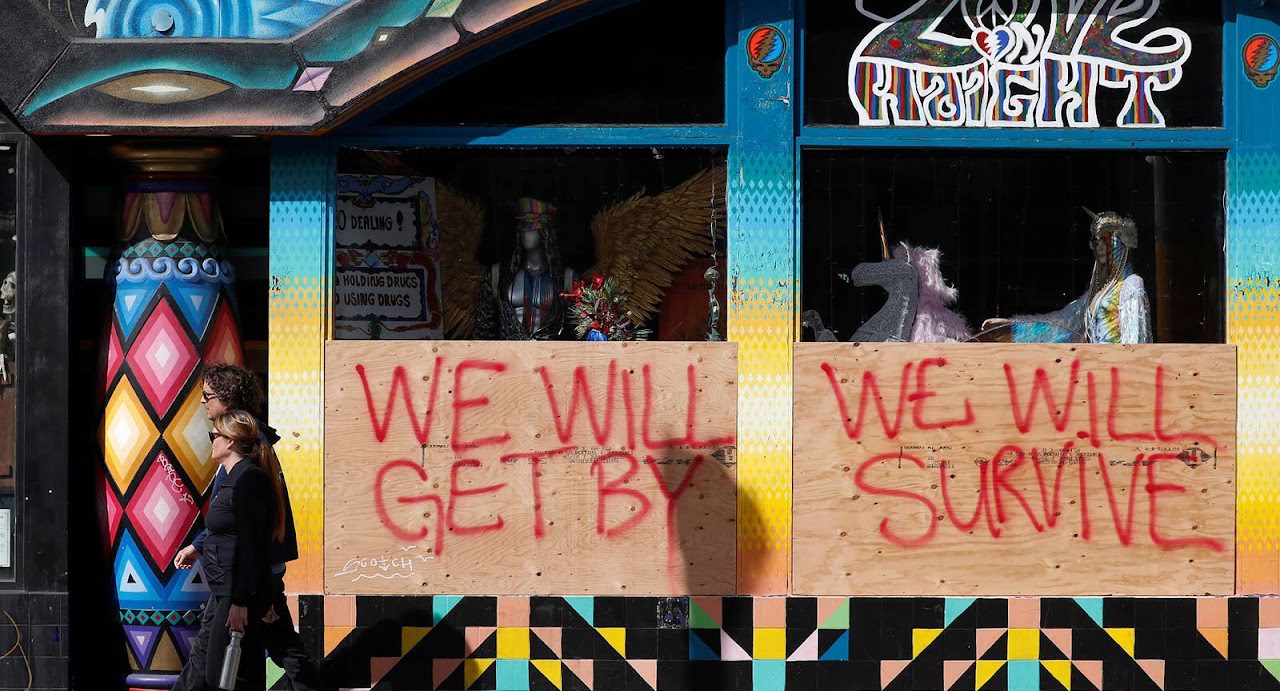 People walk past a sign during day two of the citywide shelter-in-place order in San Francisco on March 18. The sign reads: We will get by. We will survive.