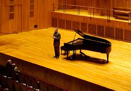 A person standing next to a piano on the stage of LeFrak Concert Hall.