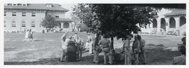 Military personnel standing and sitting on the grass at Queens College.