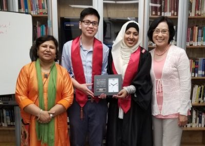 Four people posing for a group photo. The two people in the center are holding a commemorative plaque.