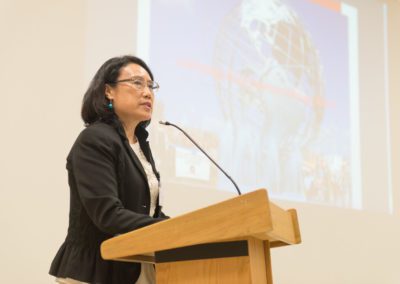 Professor Hong Wu, Associate Director of the Asian American Center, standing behind a podium and speaking into a microphone.