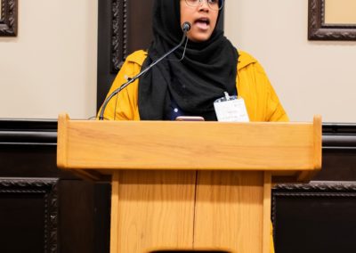 Asma talking into a microphone on a podium.