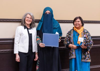 Maha standing in the center of two people hold up her certificate.