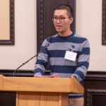 Xincheng talking into a microphone on a podium.