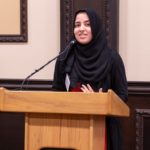 Basira talking into a microphone on a podium.