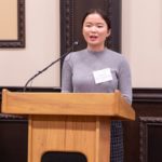 Shuqi talking into a microphone on a podium.