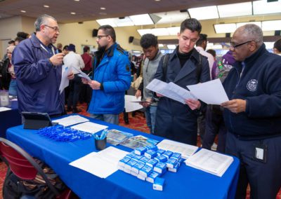 A group of people standing at a table looking at papers during a career fair.