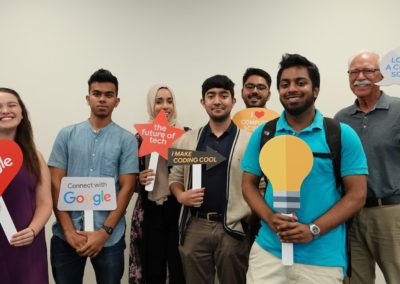 Participants of Cohort 1 posing for a photo while holding various photobooth prop signs. The signs reflect the elements of Google, Computer Science, and Computer Technology.
